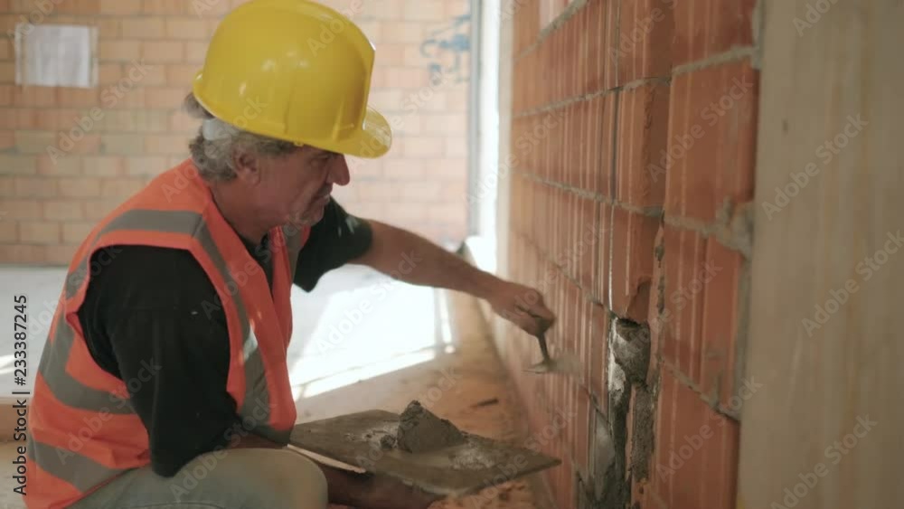 People working in construction site. Busy caucasian man at work in new house inside apartment building. White manual worker using equipment and tools to work on brick wall with cement