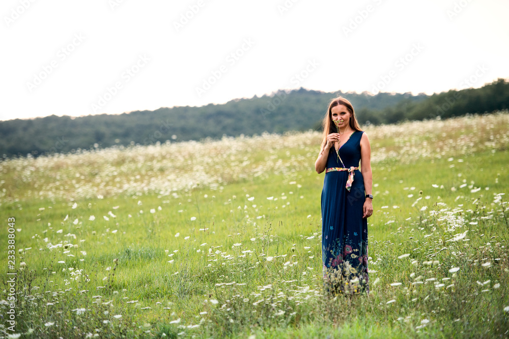 A young woman standing in nature on a summer day, smelling flowers. Copy space.