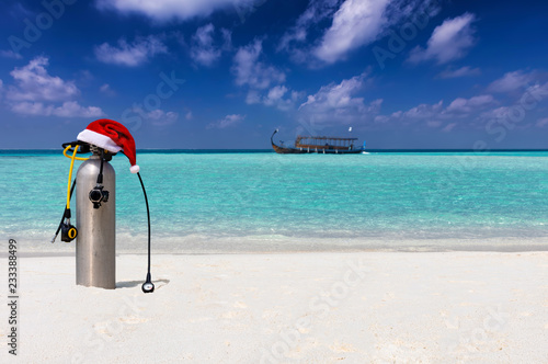 Scuba Taucherflasche mit Weihnachtsmütze am tropischen Strand mit türkisem Ozean und Taucherboot