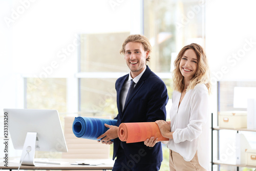Fototapeta Naklejka Na Ścianę i Meble -  Young businessman and businesswoman holding yoga mats in office. Gym after work
