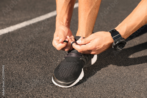 Young man tying shoelaces at stadium on sunny day