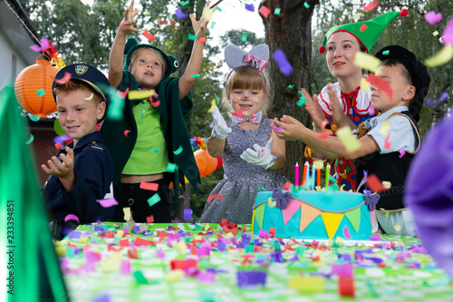 Smiling children wearing carnival costumes have fun during birthday party with cake
