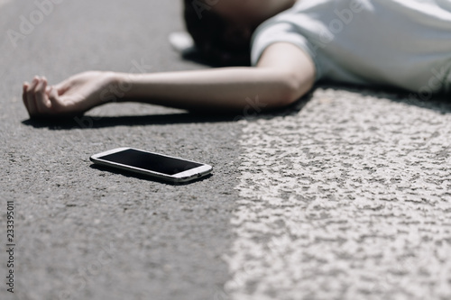 Smartphone and careless victim of traffic accident lying on a crosswalk