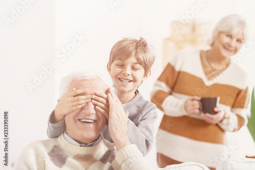 Grandson playing hide and seek with his grandfather, smiling grandmother behind them photo