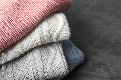 Stack of folded knitted sweaters on table, closeup. Space for text
