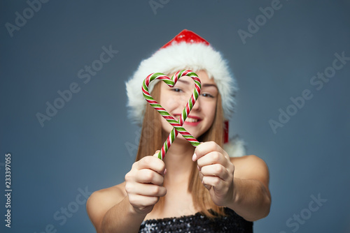 Girl in Santa hat holding Christmas candies in heart shape