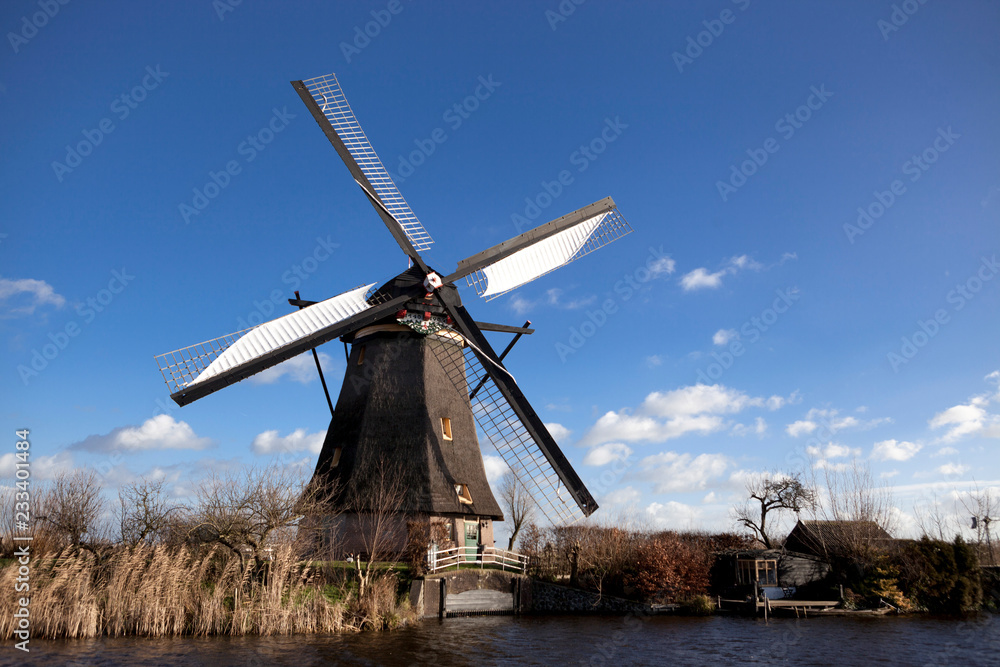Old, traditional windmill in the Dutch canals. Netherlands.White clouds on a blue sky, the wind is blowing.