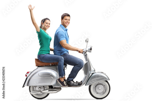 Young male and female riding on a vintage motorbike, the girl waving