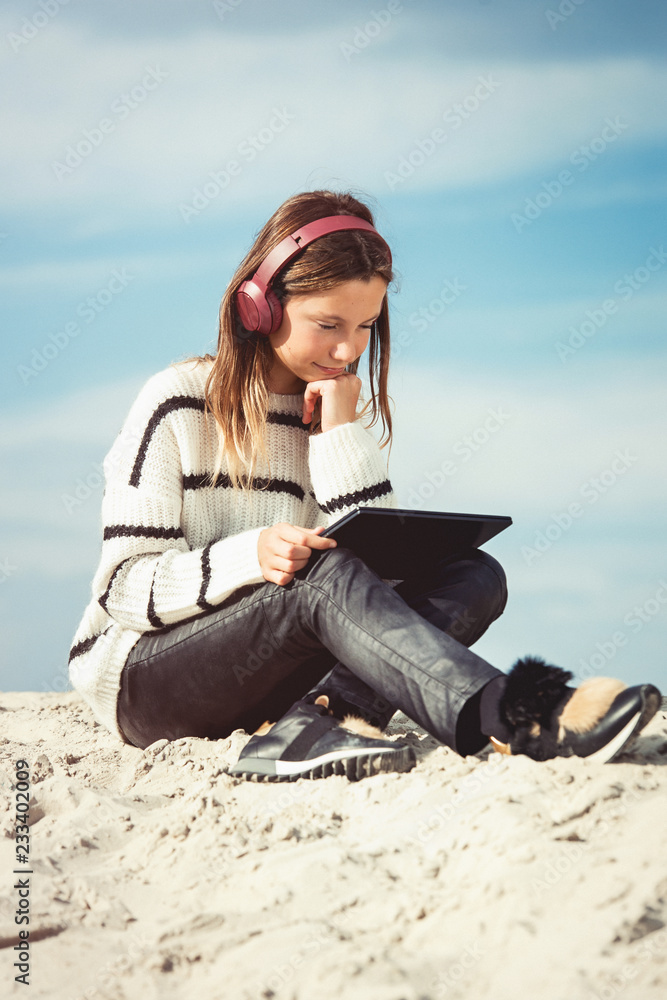 11 years girl in a wireless headphones listening to a music from a smart phone on a beach. against a blue sky. close up