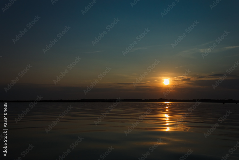 Sunset on the lake. Evening sky with beautiful clouds is reflected in the water of the lake