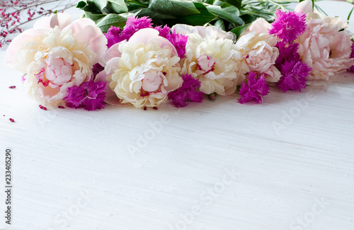 A large pile of light colors. Tender white peonies along with small bright pink carnations on a white wooden background. Floral background.
