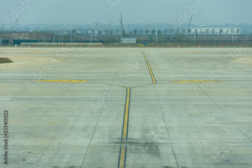 A quiet tarmac looking out to construction at a Chinese airport waiting for a plane to arrive.