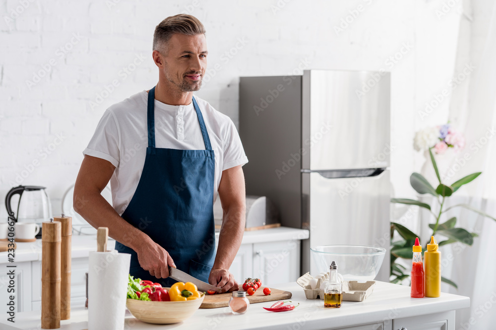 adult man cutting cherry tomatoes for salad on cutting board adult man cutting cherry tomatoes for salad on cutting board