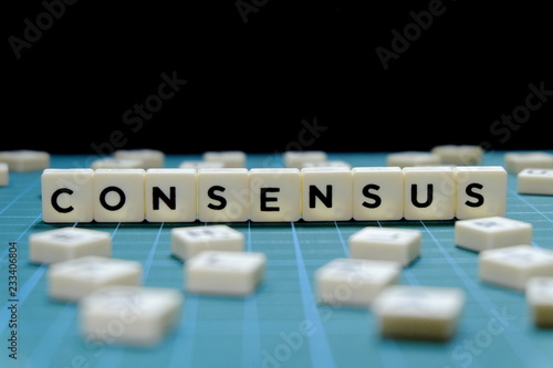 Selective focus of Consensus word made of square letter block on green square mat background.