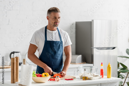 adult man standing at kitchen and making salad