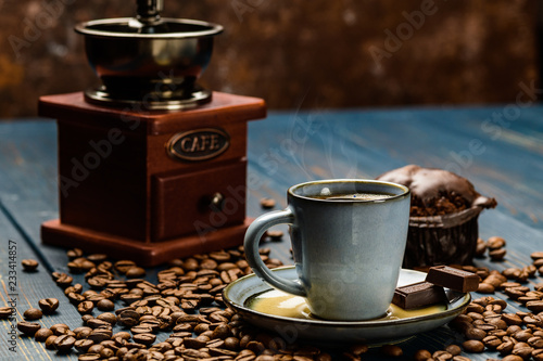 Cup of coffee on a blue wooden table with coffee beans and a chocolate