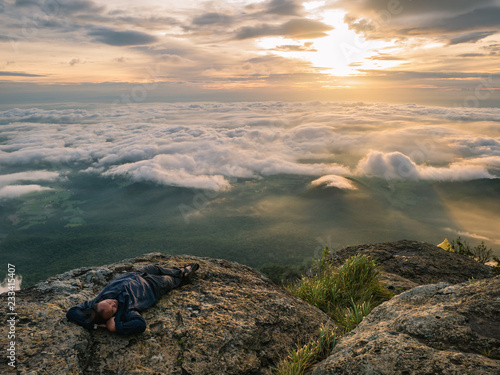 Trekker Lay down on the cliff with Beautiful Sunrise and sea of mist in the morning on Khao Luang mountain in Ramkhamhaeng National Park,Sukhothai province Thailand