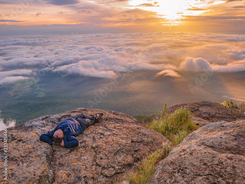 Trekker Lay down on the cliff with Beautiful Sunrise and sea of mist in the morning on Khao Luang mountain in Ramkhamhaeng National Park,Sukhothai province Thailand photo
