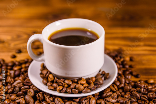 Cup of hot coffee and scattered coffee beans on wooden table