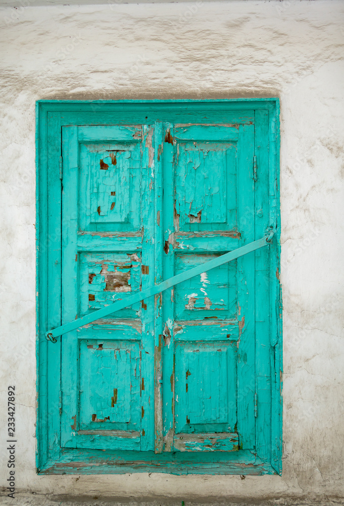 Old wooden shutters of turquoise color, paint cracked, closed with an iron crossbar. Background, white dirty wall