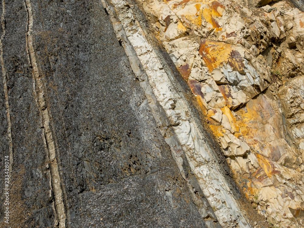 Fototapeta premium Mountain rock with gray, white and brown color stones diagonally arranged in strips. Background, macro, Caucasus