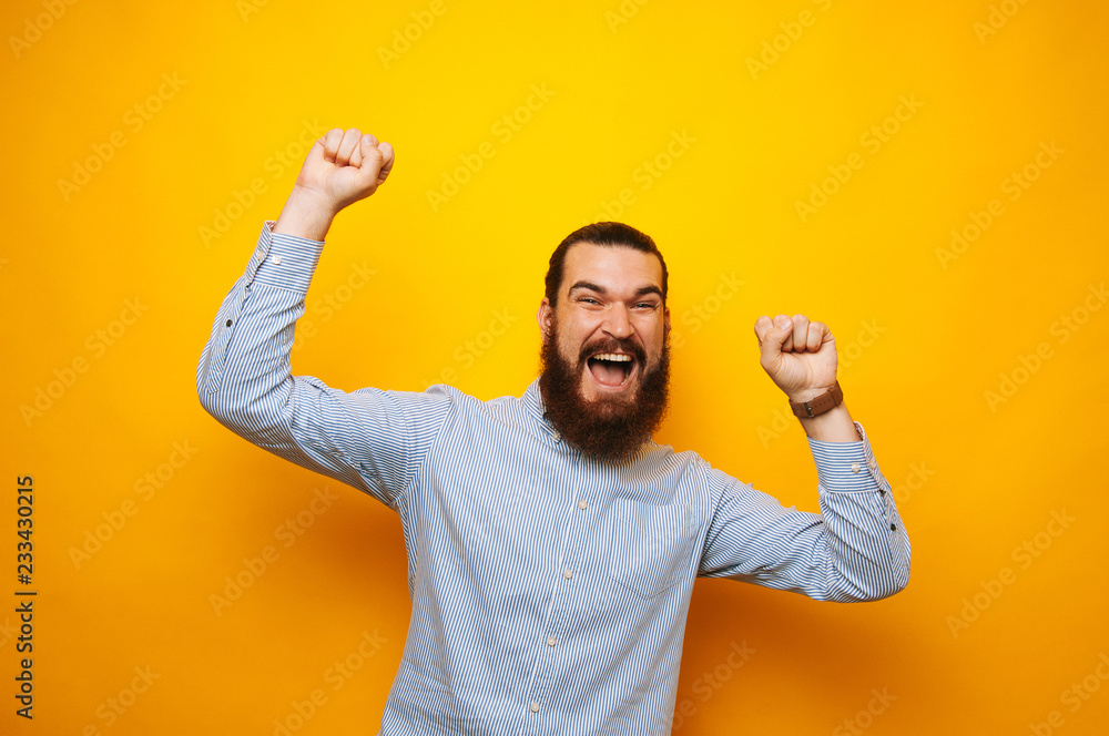 Cheerful bearded man in casual celebrating success over yellow background Cheerful bearded man in casual celebrating success over yellow background