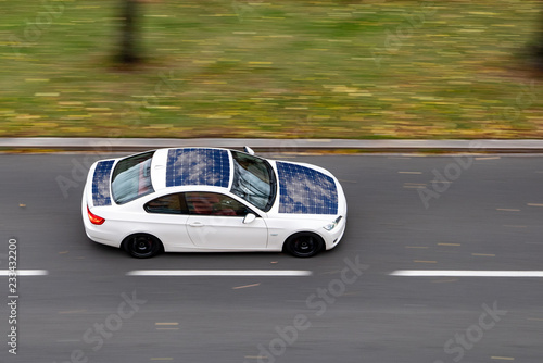 Very quickly driving white ecological solar car on a city street
