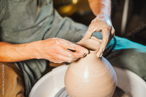 Unknown craftsman creates jug. Focus on hands only. Small business, talent, inspiration concept. Overhead view. Working process of man's work at potters wheel in art studio