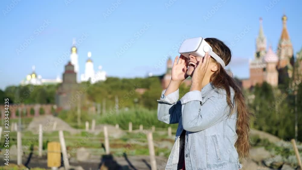 Casual modern brunette standing in summer green park on urban background. Woman wearing VR headset, turning around and smile Casual modern brunette standing in summer green park on urban background. Woman wearing VR headset, turning around and smile