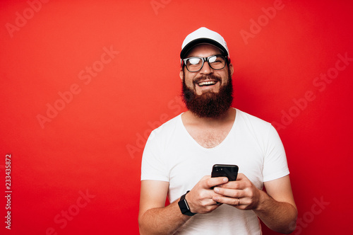 Smiling happy man using phone over red background and looking at the camera © Vulp