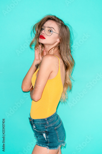 Studio shot of a very attractive woman in yellow top and denim shorts on blue background © Roberto Vivancos