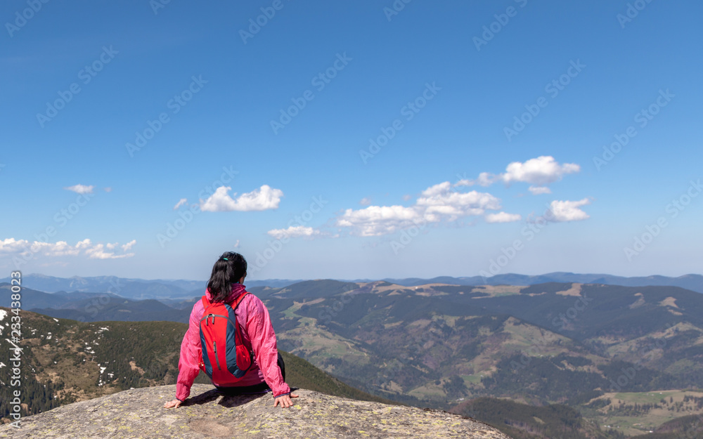 Fototapeta premium A girl with a backpack sitting on a large rock in the mountains. The concept of travel