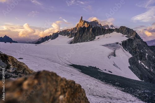 Stunning sunset view of an alpine landscape in Mont Blanc massif. Famous alpine peak Dent du Geant (Dente del Gigante) in purple evening colors. Alpinism and climbing on glacier in the Alps, Chamonix.