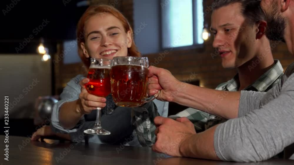 Group of young friends enjoying drinks at the bar. Sliding shot of cheerful people toasting with their drinks, enjoying beer together at the local pub. Beautiful woman and her male friends partying. Group of young friends enjoying drinks at the bar. Sliding shot of cheerful people toasting with their drinks, enjoying beer together at the local pub. Beautiful woman and her male friends partying.