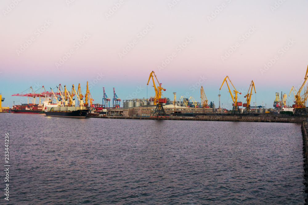 Port with cargo containers and cranes, removing these containers from ships at sunset