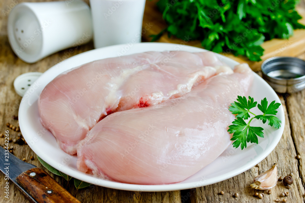 Raw chicken breast fillets on plate on wooden table close up Raw chicken breast fillets on plate on wooden table close up