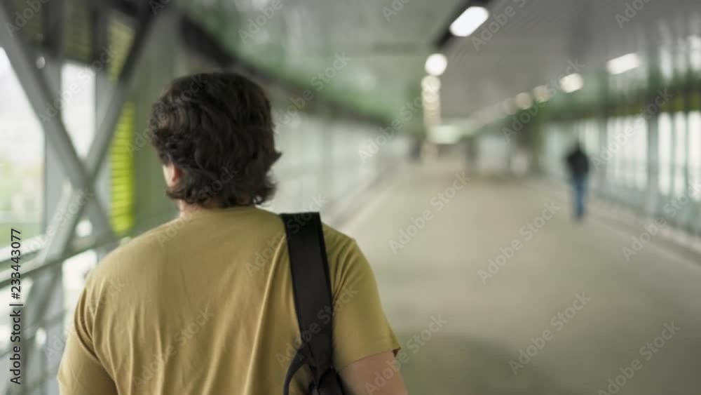 Rear view of young caucasian man with dark hair wearing beige t shirt and backpack walking in the tunnel. Tracking slow motion medium shot Rear view of young caucasian man with dark hair wearing beige t shirt and backpack walking in the tunnel. Tracking slow motion medium shot