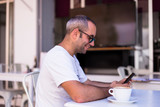 Male hands holding smartphone with cup of coffee on table in a terrace. Daytime, lifestyle