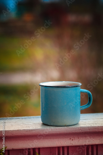 Old mug with a hot drink on a wooden stump in the outdoors. Photo in vintage color image style. Coffee break outdoors. Morning Still life. Morning at the campsite.