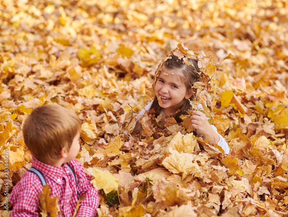 Fototapeta premium Children are lying and playing on fallen leaves in autumn city park.