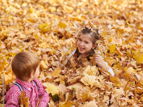Children are lying and playing on fallen leaves in autumn city park.