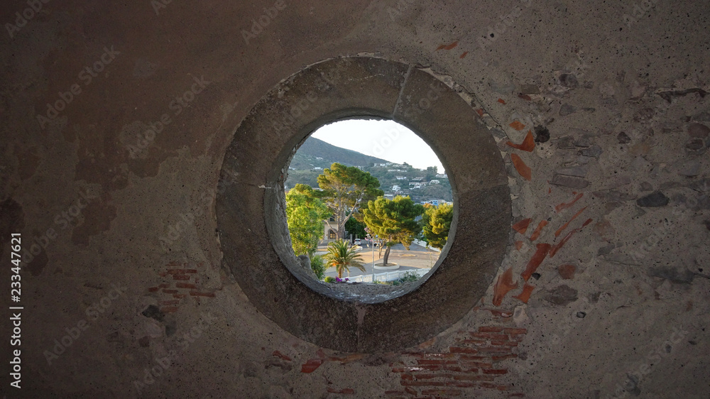 Blick durch ein rundes Fenster in einer Steinmauer