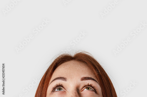 Close-up young red-haired girl isolated on gray background in white t-shirt. She looks in up.