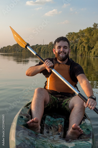 Young bearded man sitting with paddle in kayak in the middle of the lake