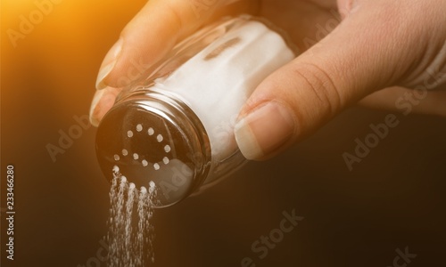 Female hand pouring salt from salt shaker on black background