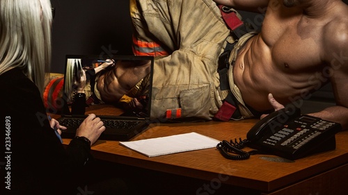 sexy firefighter lying on an office in front of a blond women