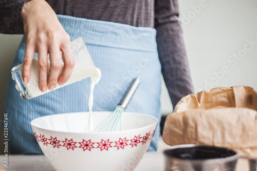 Young woman adding a milk to the egg mixture.making dough for the cake. selective focus.