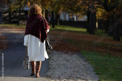 Stylish woman in autumn clothing walking down a path in autumn with the low sunlight illuminating her from the side