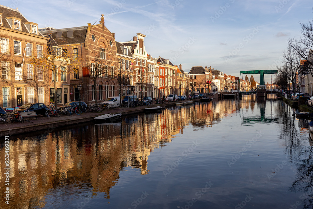 Drawbridge at sunset over a canal in Leiden with classic facades against a blue sky with the scene doubled as a reflection in the water