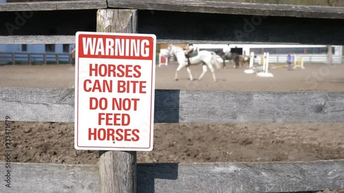 Warning. Horses can bite sign on fence with horses and riders in background. Toronto. photo